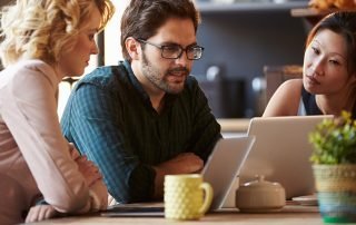 Three Businesspeople Working At Laptop In cafe